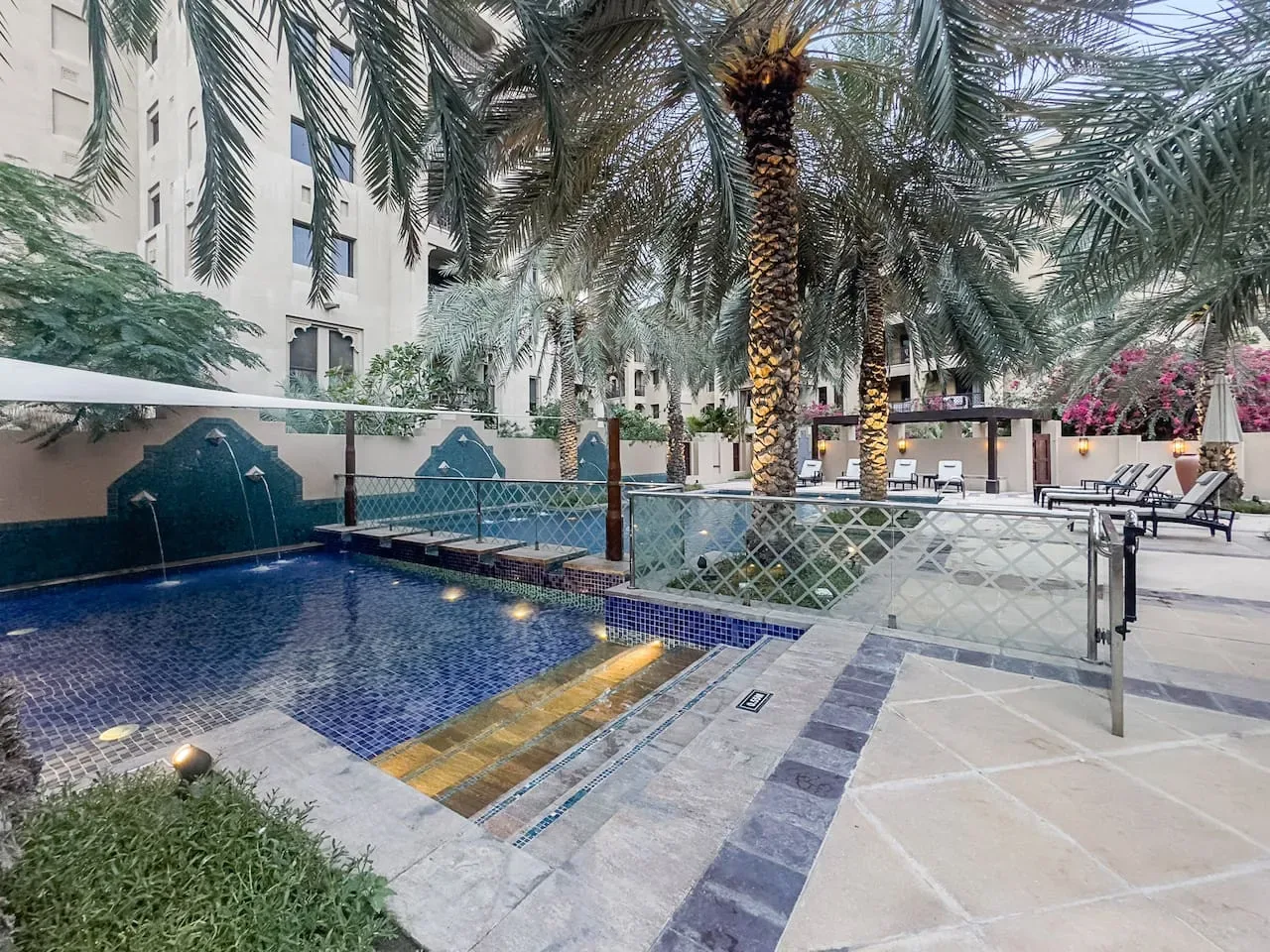 Una piscina al aire libre con escalones de azulejos, palmeras y una terraza pavimentada.