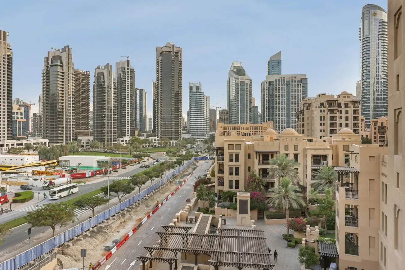 Un horizonte urbano se alza sobre una carretera bordeada de palmeras y edificios bajos.
