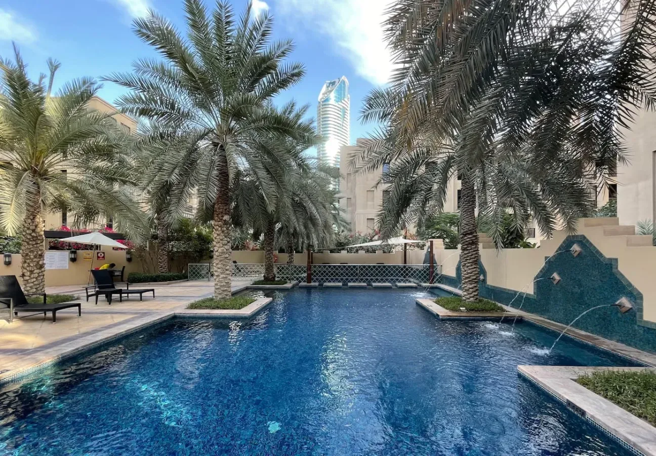 Una piscina al aire libre está rodeada de palmeras y asientos para descansar.