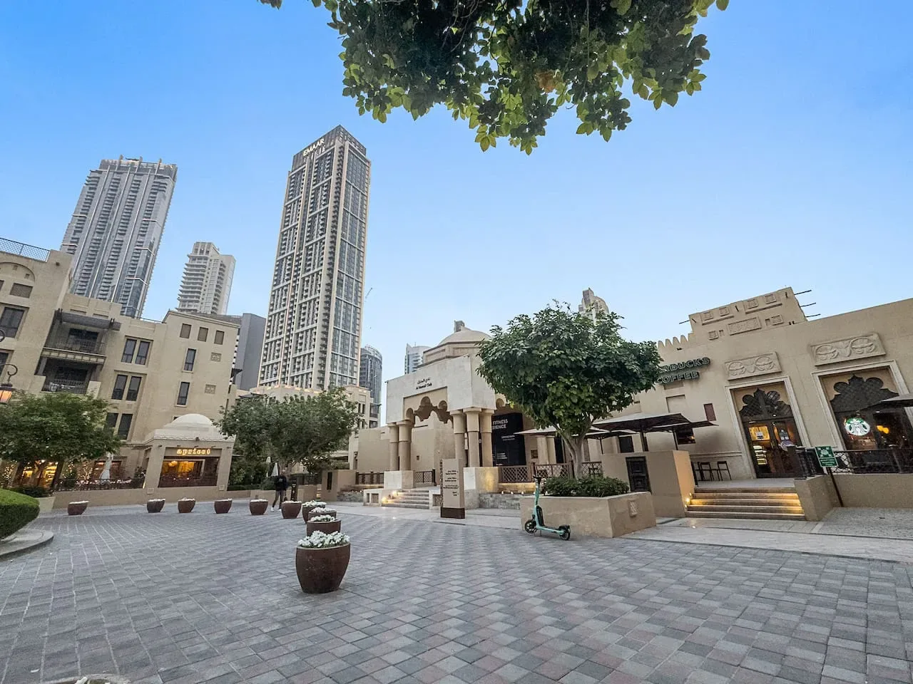 Una plaza pavimentada al aire libre con tiendas y edificios altos bajo un cielo despejado.