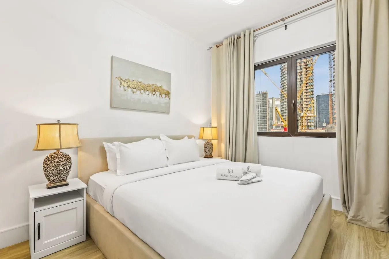 Un dormitorio luminoso con una cama bien arreglada y una ventana con vistas a edificios cercanos.
