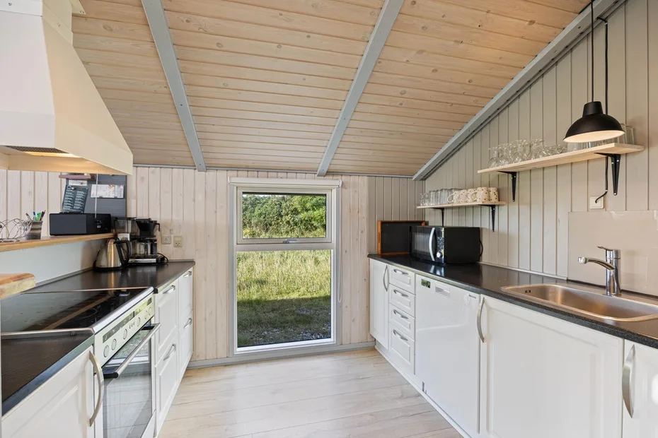 Una cocina luminosa con gabinetes blancos, encimeras oscuras y una ventana con vista a la vegetación.