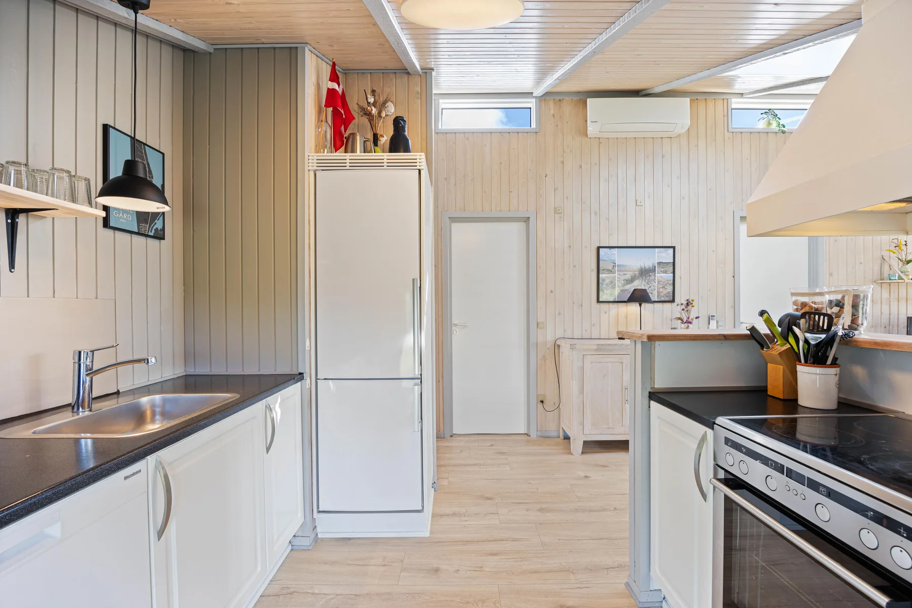 Una cocina luminosa con encimeras oscuras, gabinetes blancos y un refrigerador central.