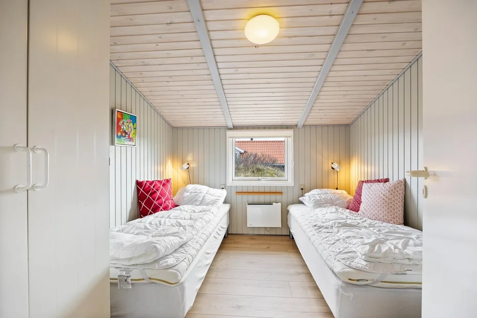 Un dormitorio luminoso con dos camas individuales y una ventana al fondo.