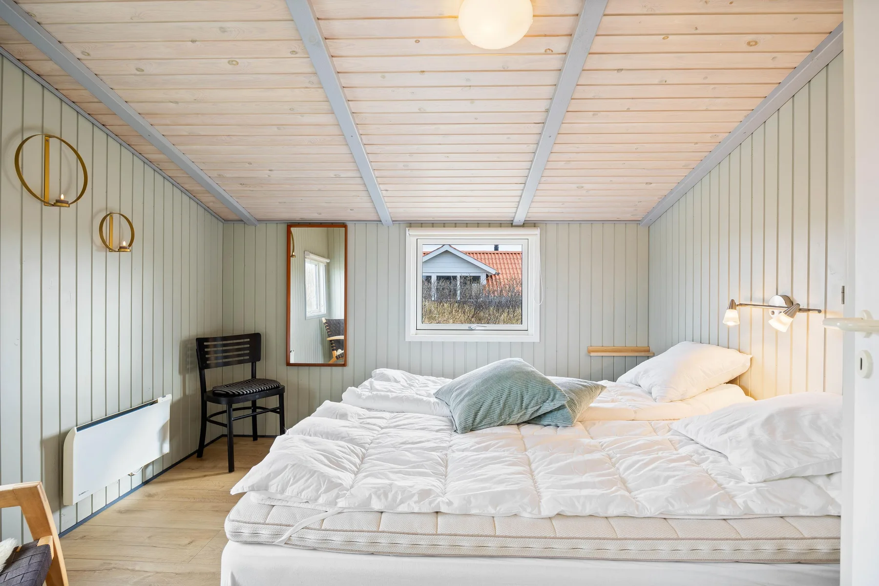Un dormitorio con una cama vestida de blanco y una ventana con vistas a una casa cercana.