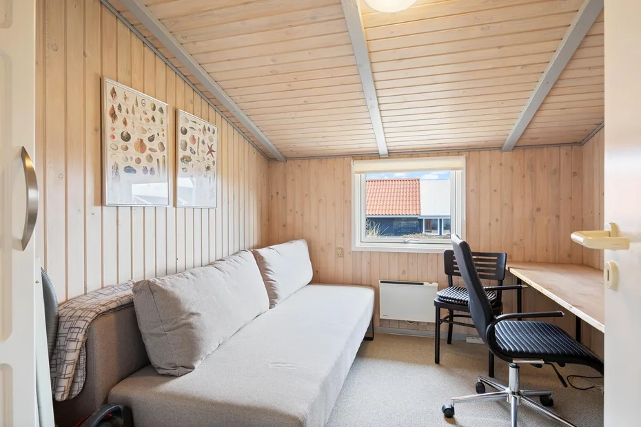 Una habitación revestida de madera con sofá, escritorio y sillas junto a una ventana.