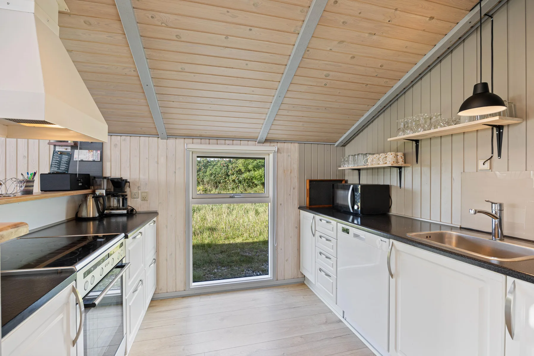 Una cocina luminosa con gabinetes blancos, encimeras oscuras y una puerta de vidrio con vista a la vegetación.