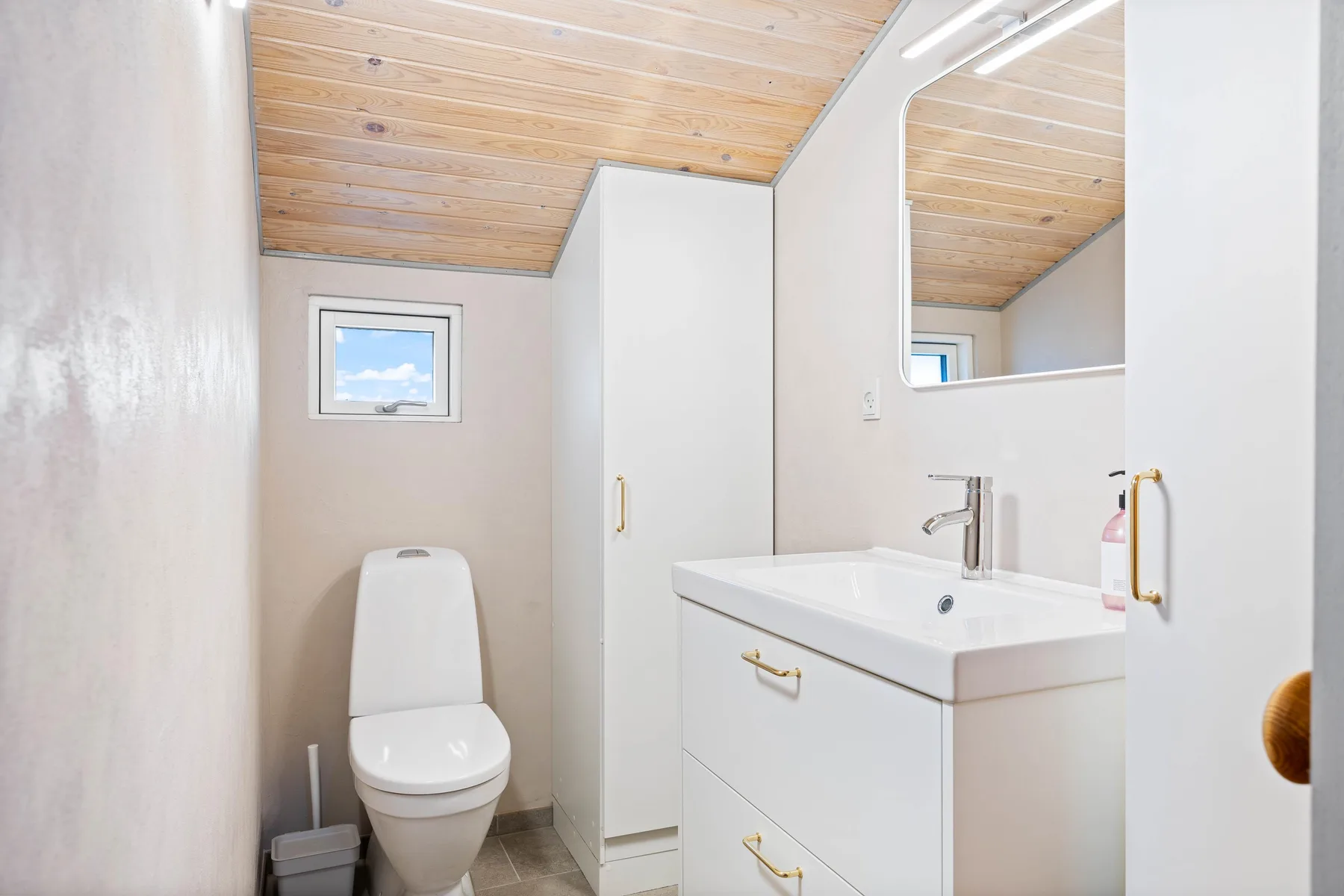 Un baño con inodoro, lavabo y techo inclinado de madera.