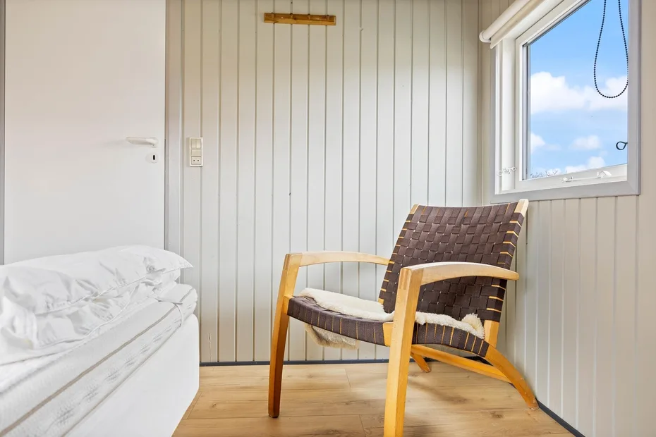 Un rincón de dormitorio con una cama, un sillón de madera y una ventana.