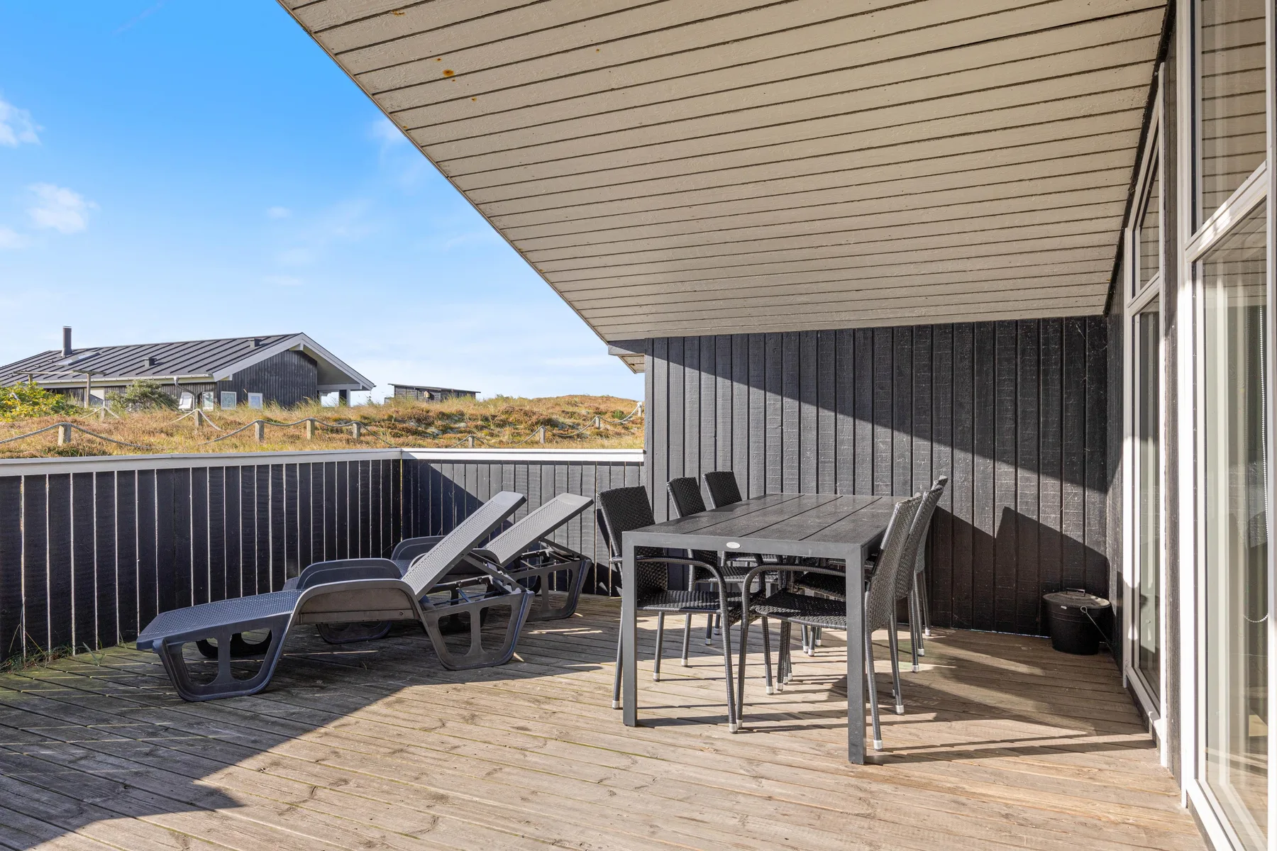 Una terraza cubierta tiene asientos exteriores, una mesa de comedor y vistas al paisaje circundante.