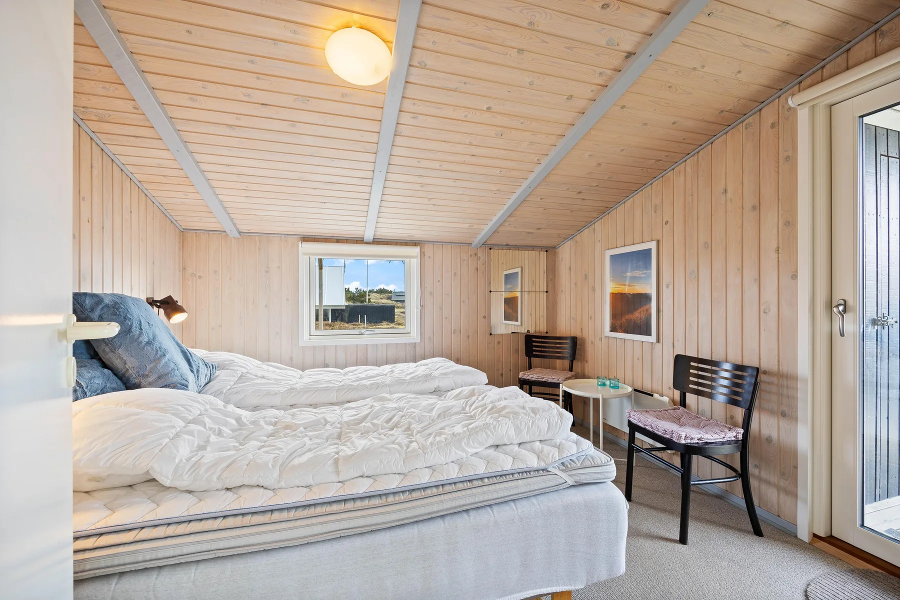 Un dormitorio con una cama, paredes revestidas de madera y una ventana.