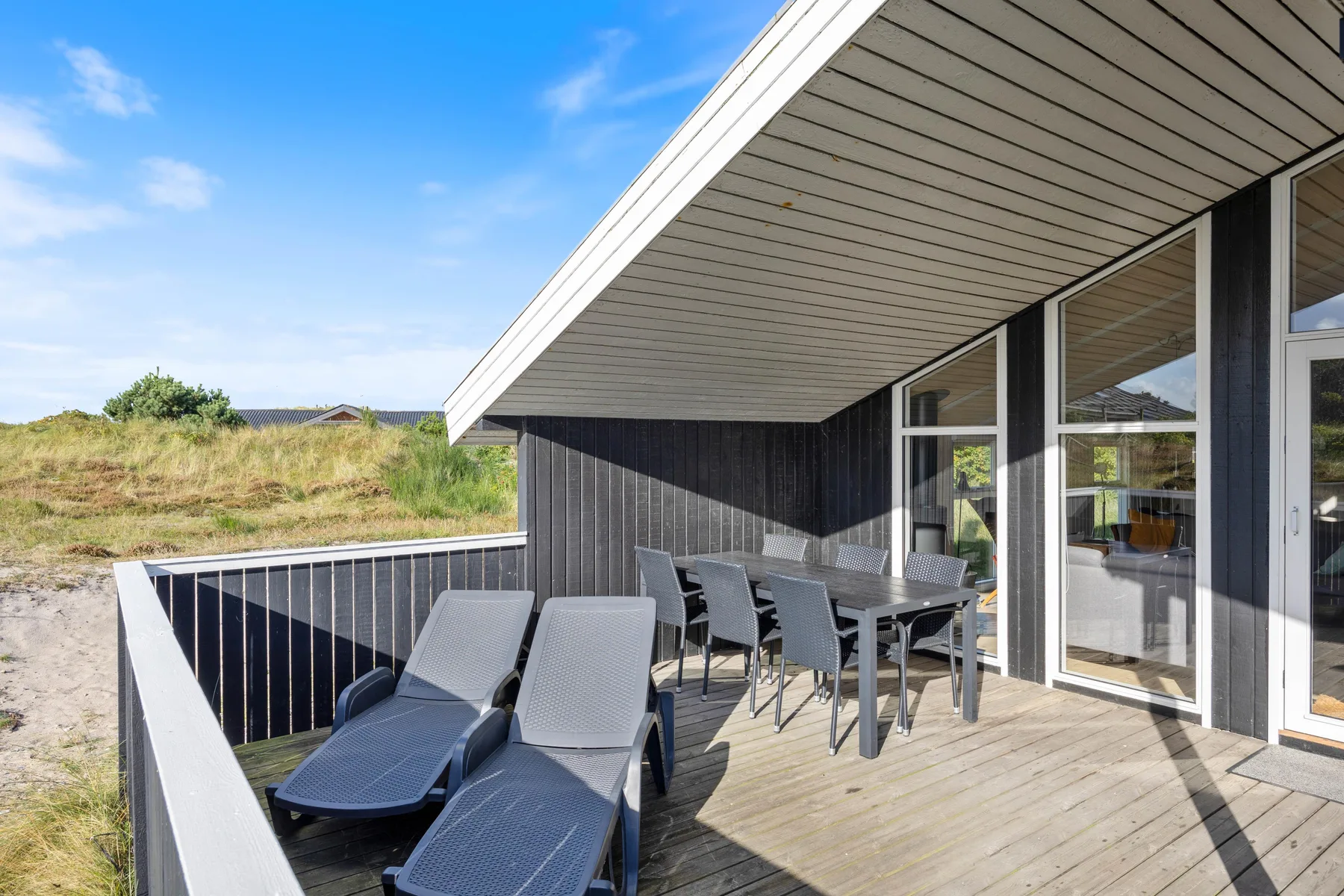 Una terraza exterior tiene asientos reclinables y una mesa de comedor junto a grandes ventanas.