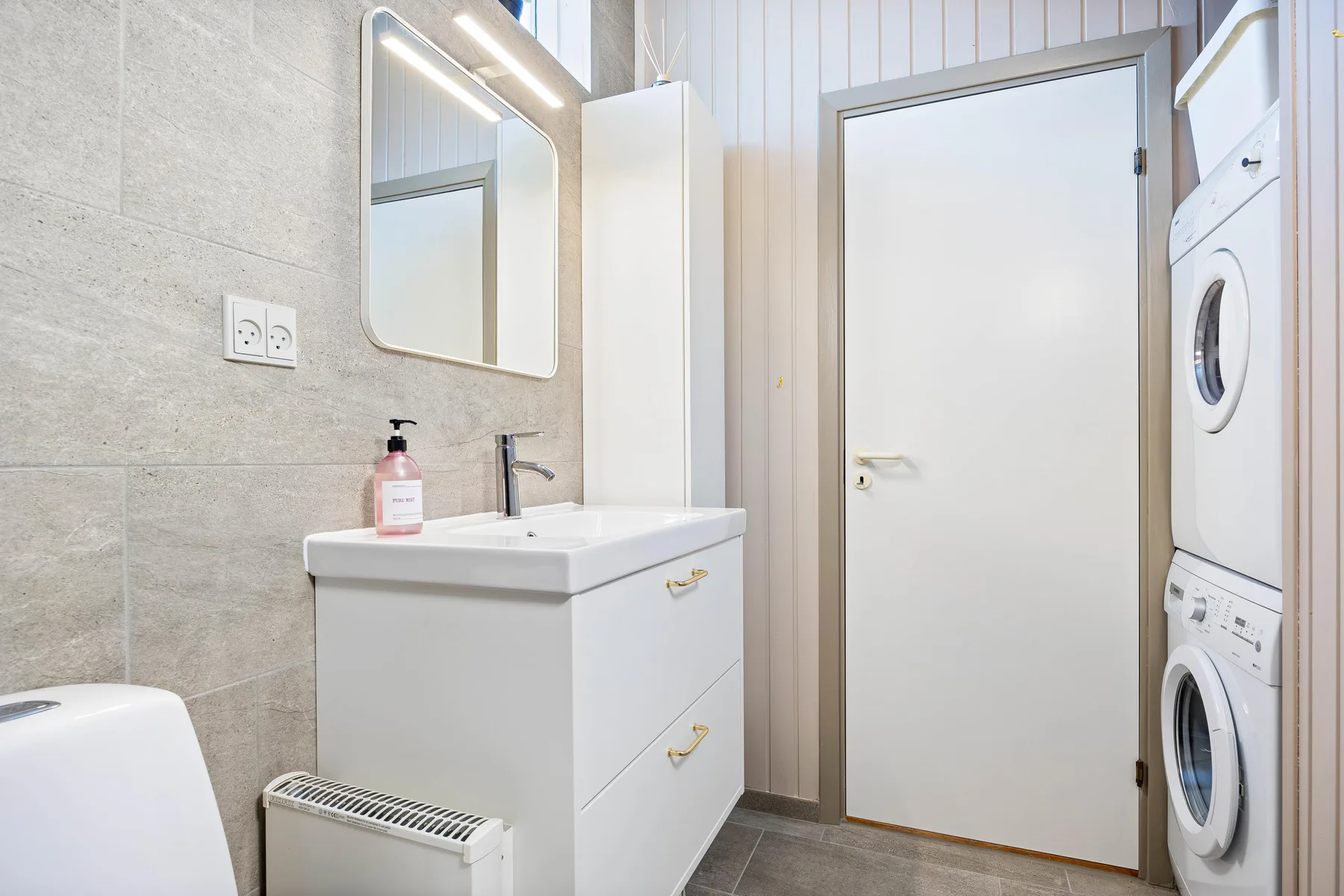Un baño luminoso con lavabo, espejo y lavadora y secadora apiladas.