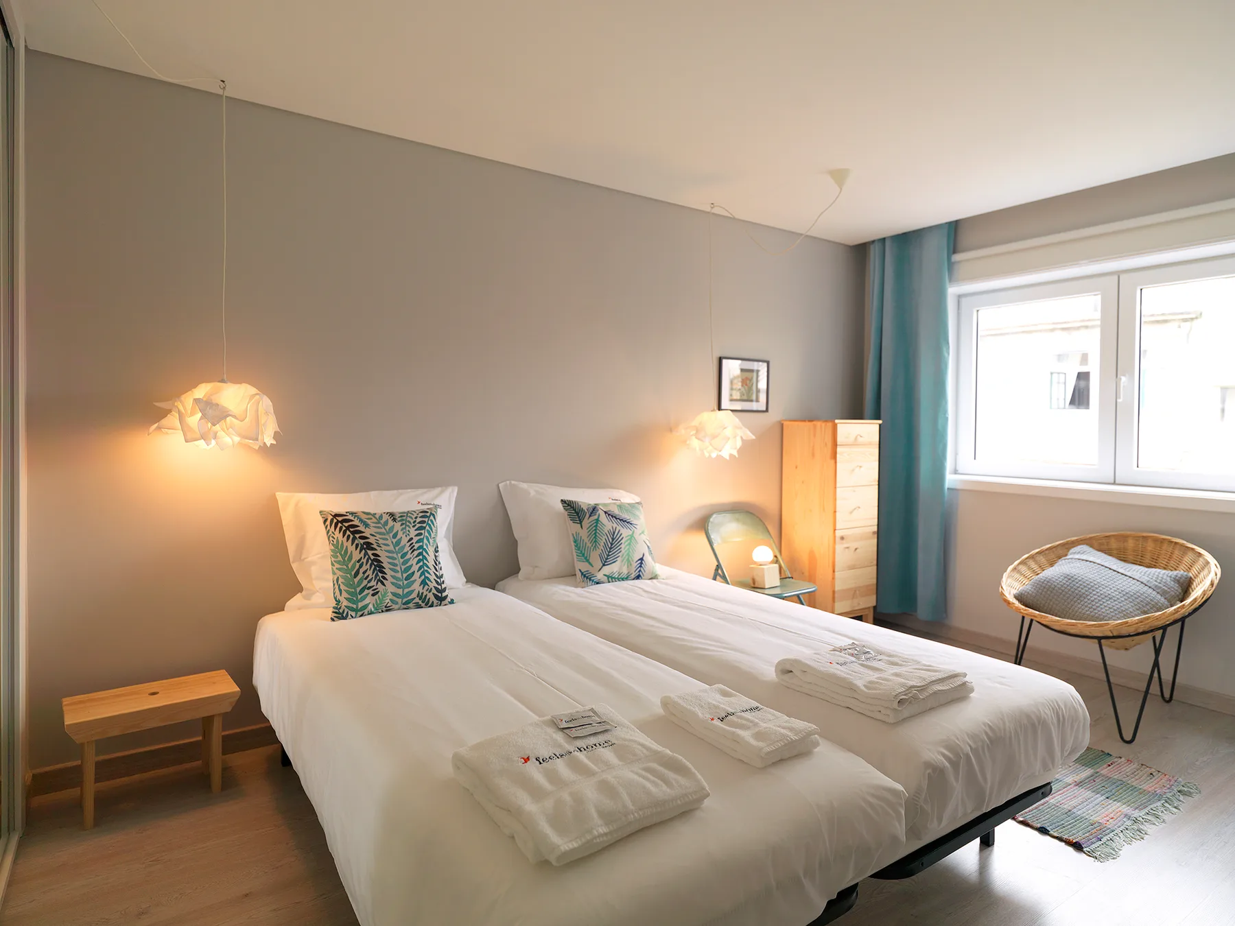 A bright bedroom with two beds, bedside tables, and a large window.