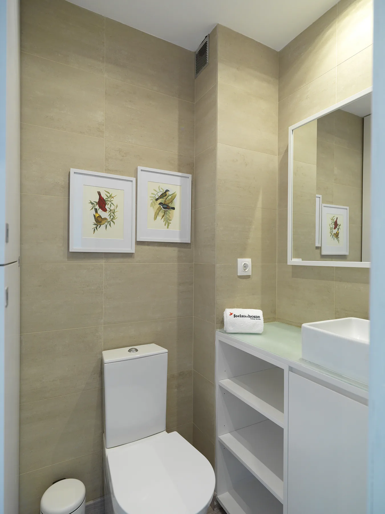 A tiled bathroom with a toilet, sink, and framed botanical prints.