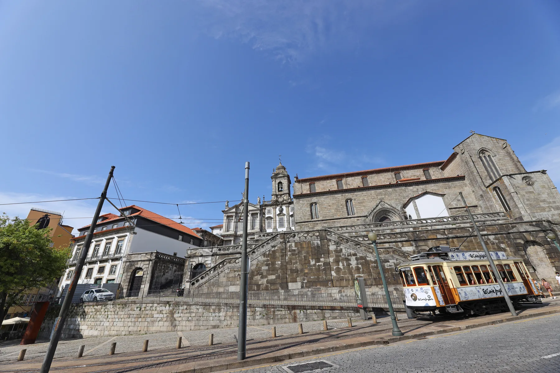 A stone church stands beside a city street with a tram passing in front.