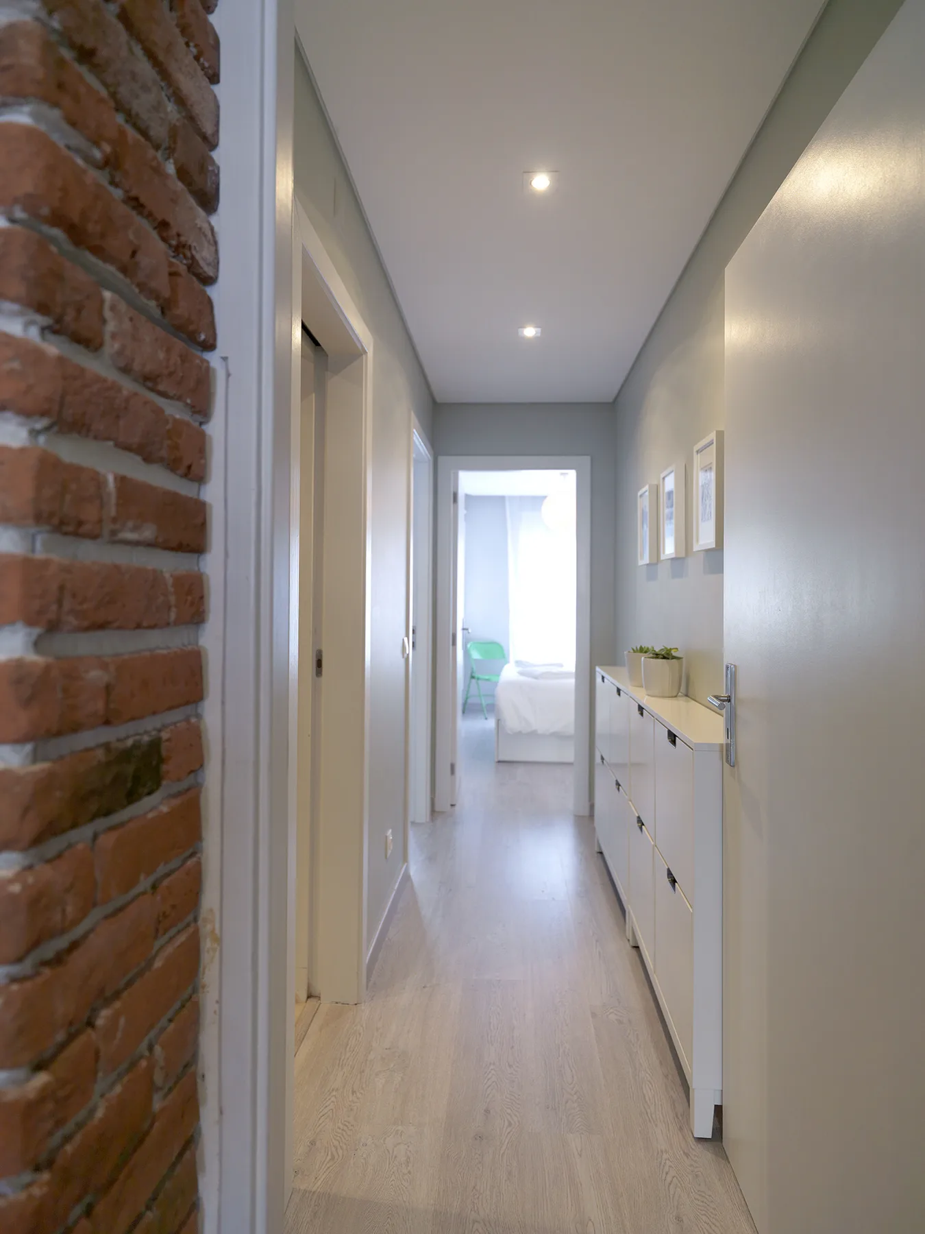 A bright apartment hallway with a long cabinet and a bedroom visible at the end.