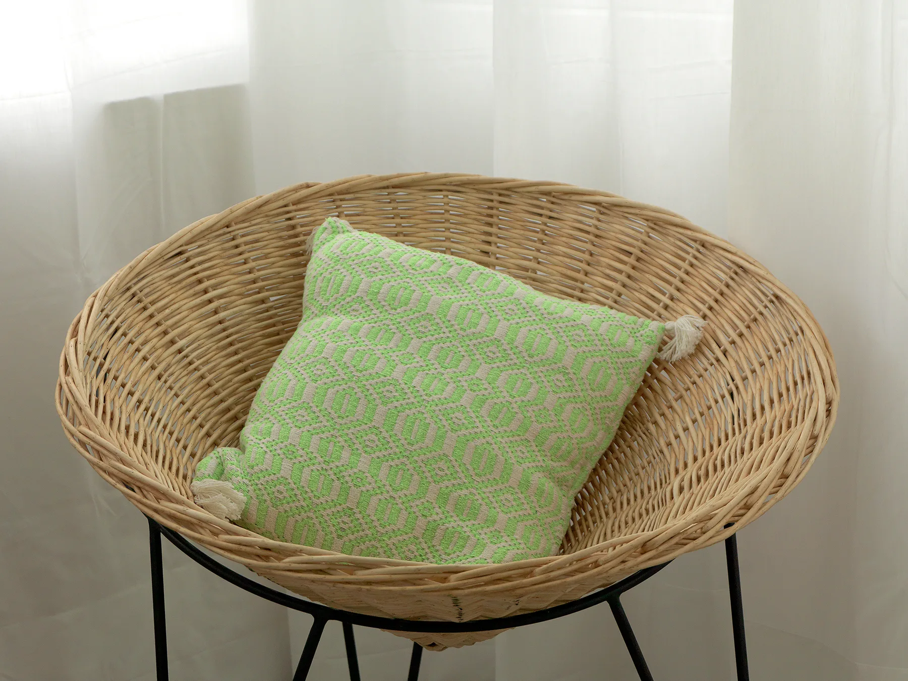 A wicker seating area with a green patterned cushion sits by a bright window.