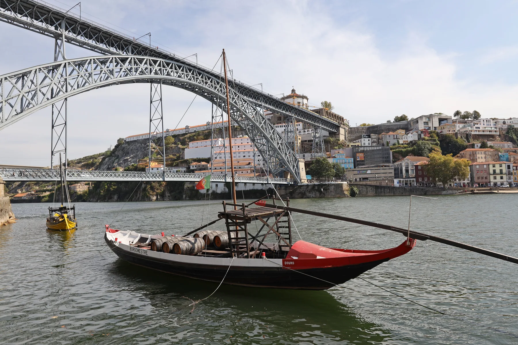 A river scene with a traditional boat beneath a large metal bridge.