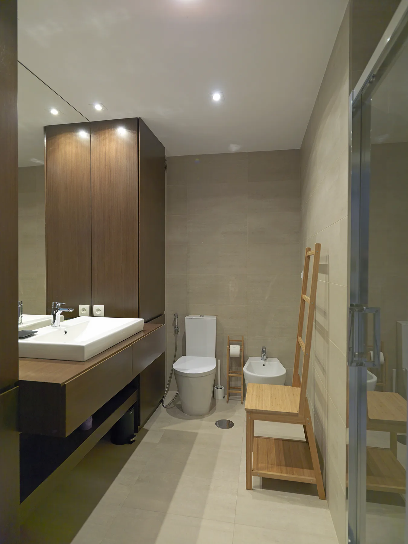 A tiled bathroom with a sink, toilet, bidet, and glass shower enclosure.