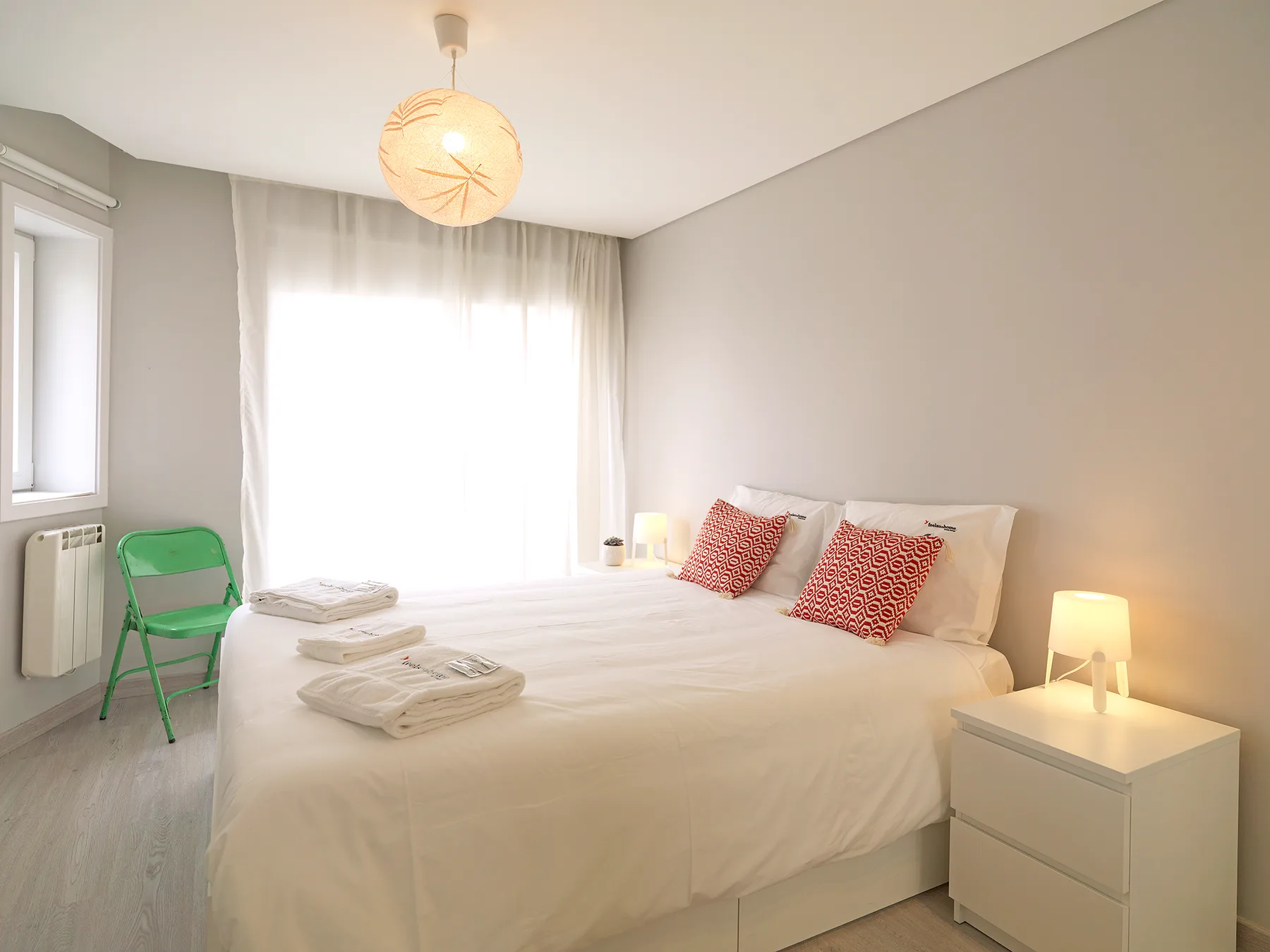 A bright bedroom with a neatly made bed and a green chair by the window.