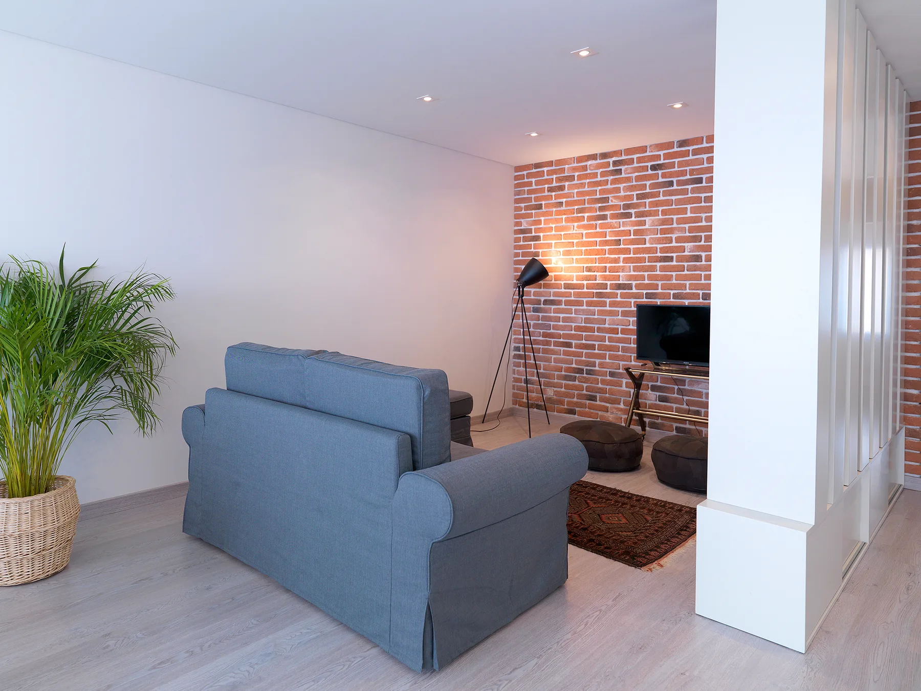 A living room with blue seating, a brick accent wall, and a television.