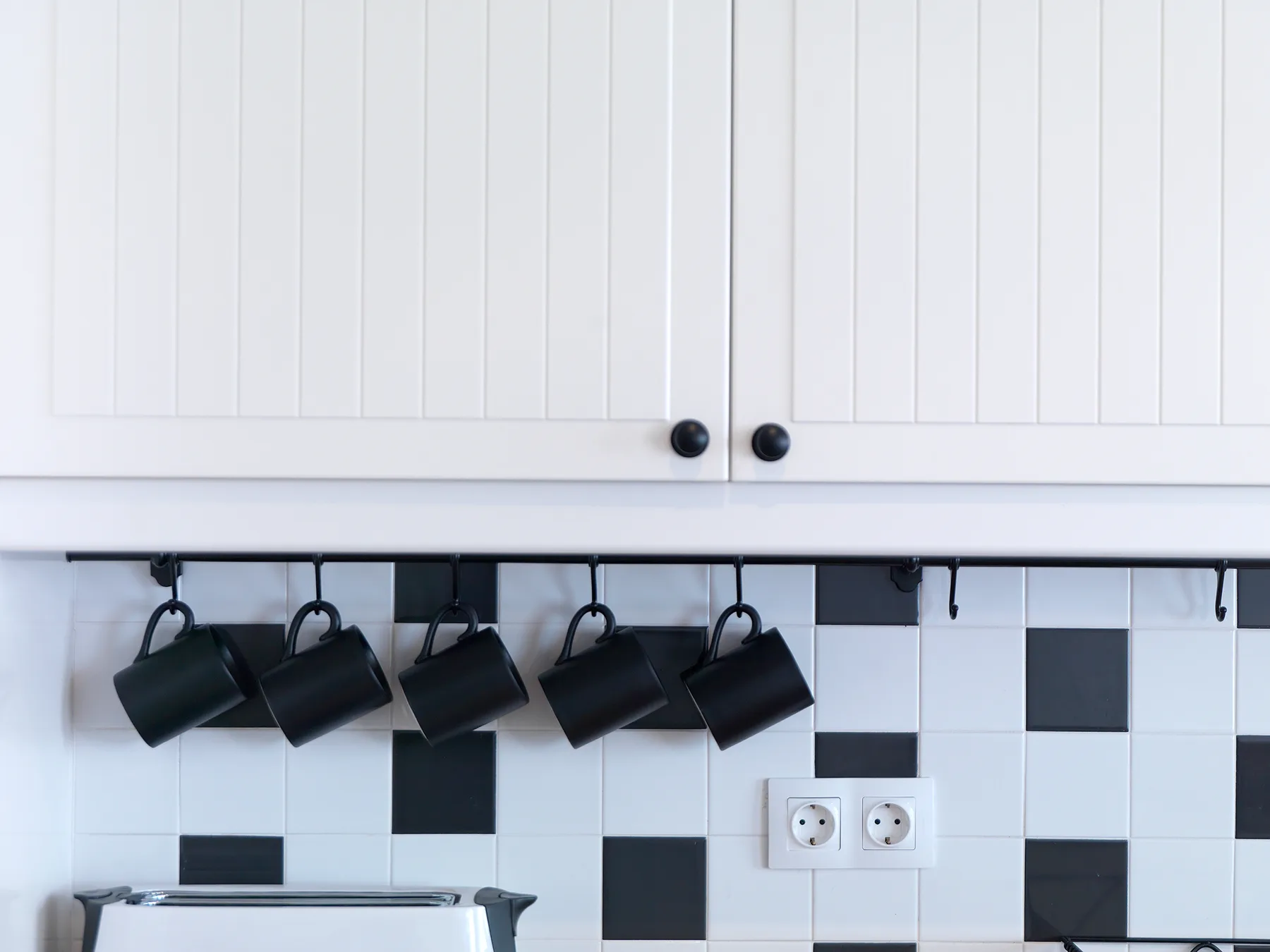 A tiled kitchen backsplash sits below white cabinets, with black hanging lights and electrical outlets.