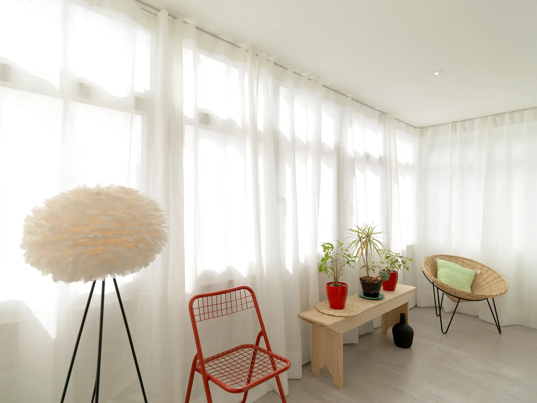 A bright sitting area with sheer curtains, a red chair, and potted plants.