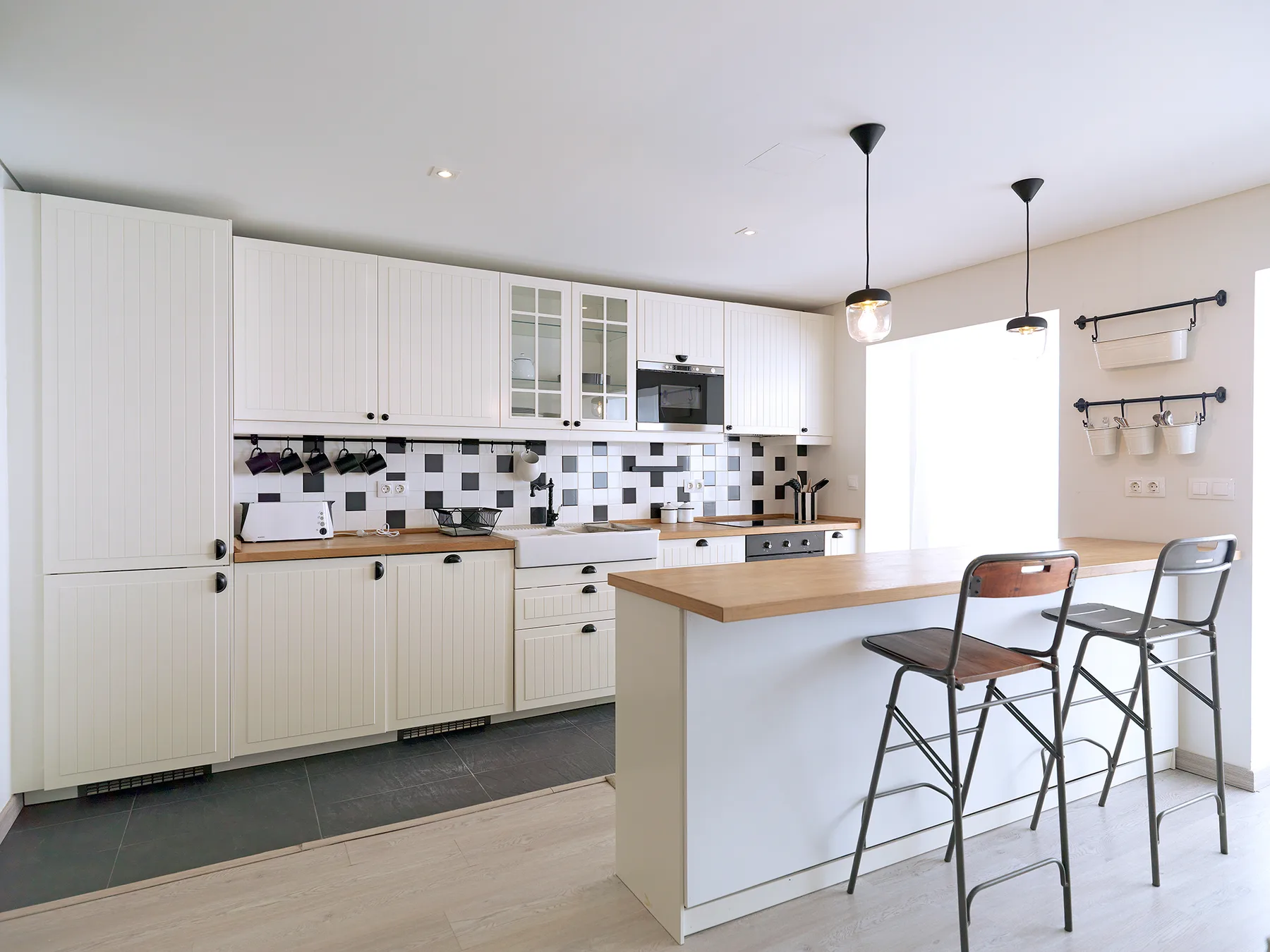 A bright kitchen with white cabinets, a tiled backsplash, and a breakfast counter.