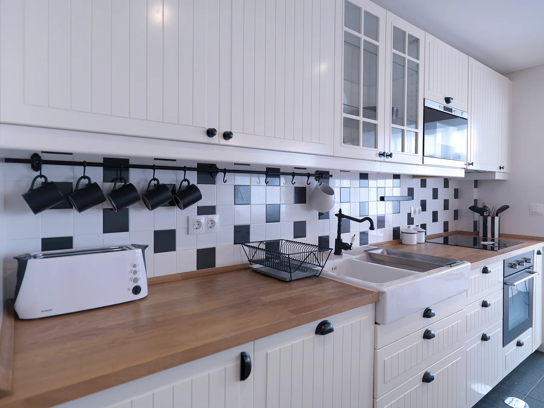A bright kitchen with white cabinets, a wood countertop, and a tiled backsplash.