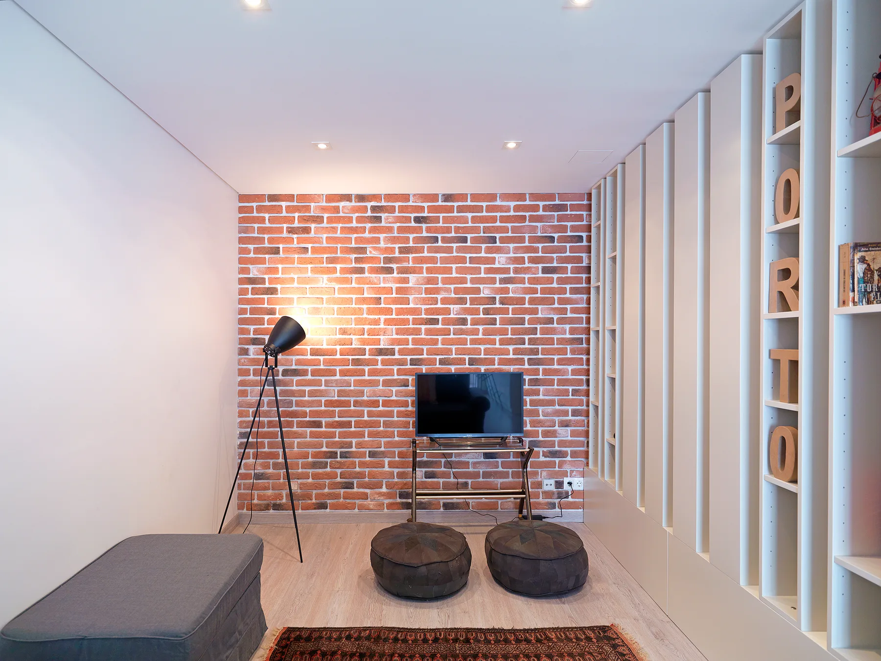 A living room with a television, floor lamp, and two round ottomans.