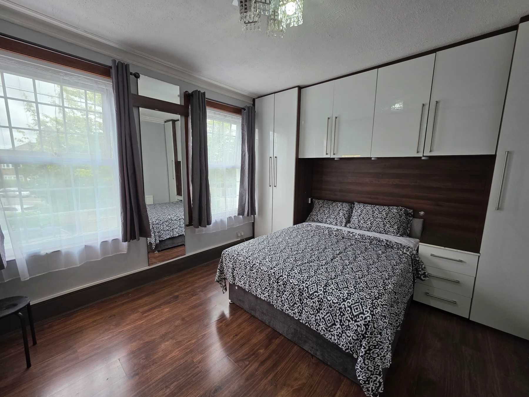 A bedroom with a double bed, built-in cabinets, and large curtained windows.