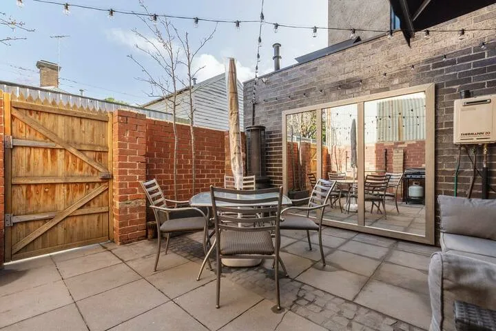 An outdoor patio with a dining table and seating beside brick walls and a wooden gate.