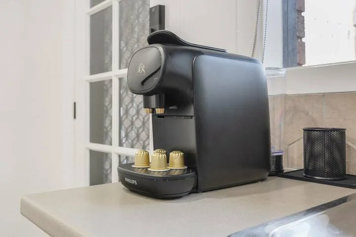 A black espresso machine sits on a kitchen counter beside a window.