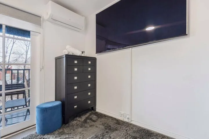 A bedroom with a dark dresser, blue seat, and wall-mounted television.