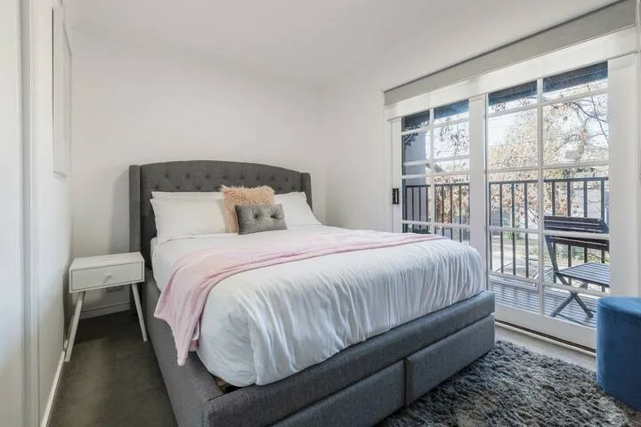 A bright bedroom with a neatly made bed beside large windows.