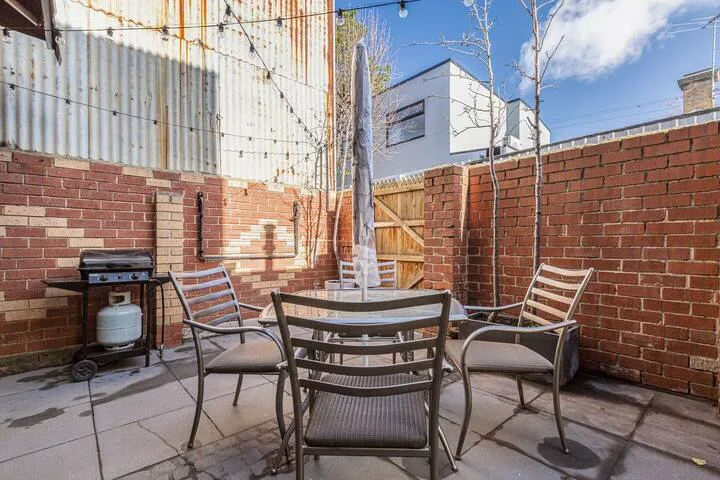 A paved outdoor patio with a dining table, seating, and a barbecue grill.
