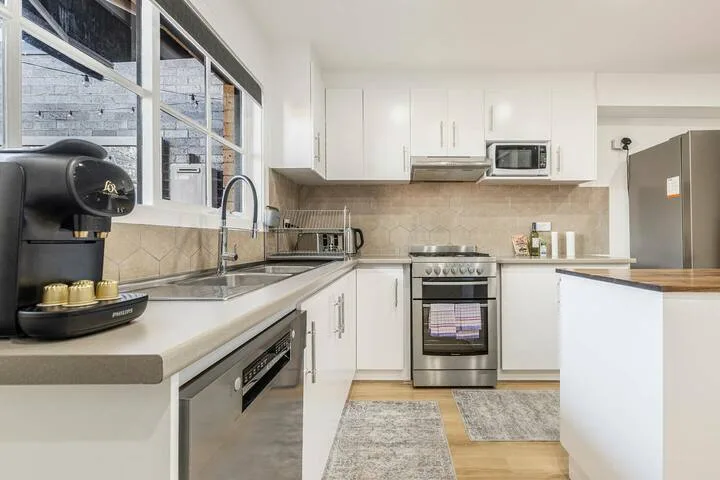 A bright kitchen with white cabinets, a stainless steel stove, and a coffee machine.