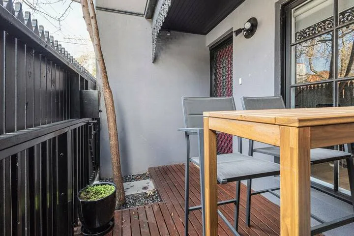 A small outdoor seating area with a wooden table beside a black fence.