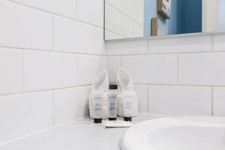 Bathroom toiletries sit on a counter beside a tiled wall and mirror.