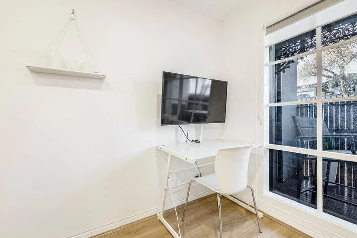 A bright room with a wall-mounted television, desk, and large window.