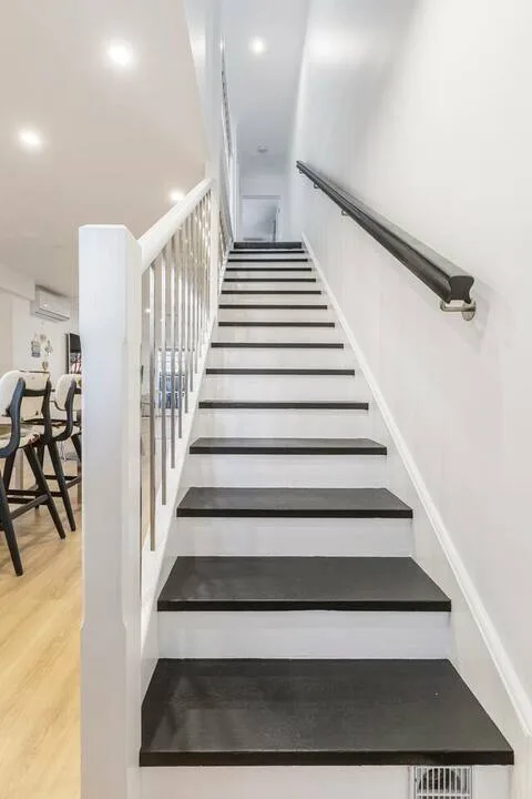 A staircase with dark steps rises beside a white railing.