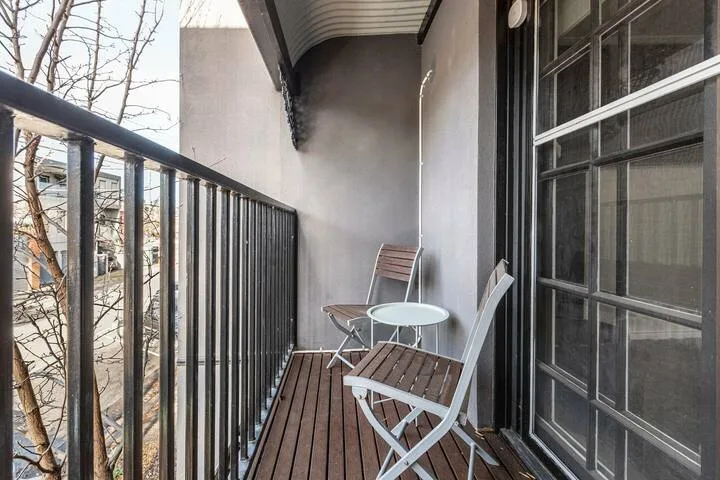 A narrow balcony with outdoor seating beside large glass doors.
