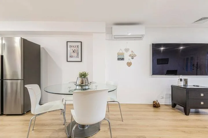 Dining area with a glass table and seating beside a wall-mounted television.