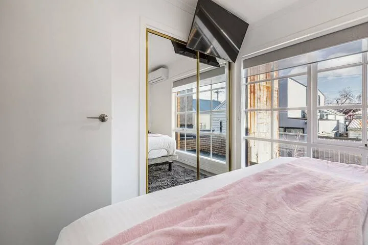 A bright bedroom with a bed, mirrored closet doors, and large windows.