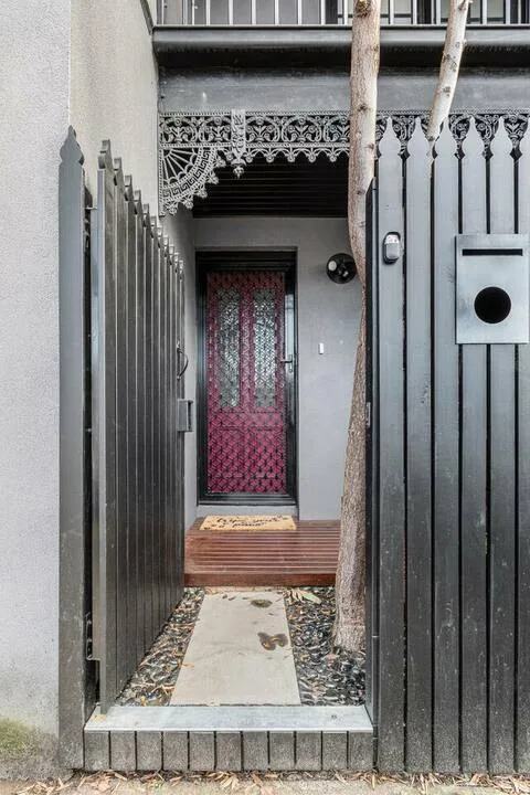 A narrow gated entrance leads to a patterned red door beneath decorative metalwork.