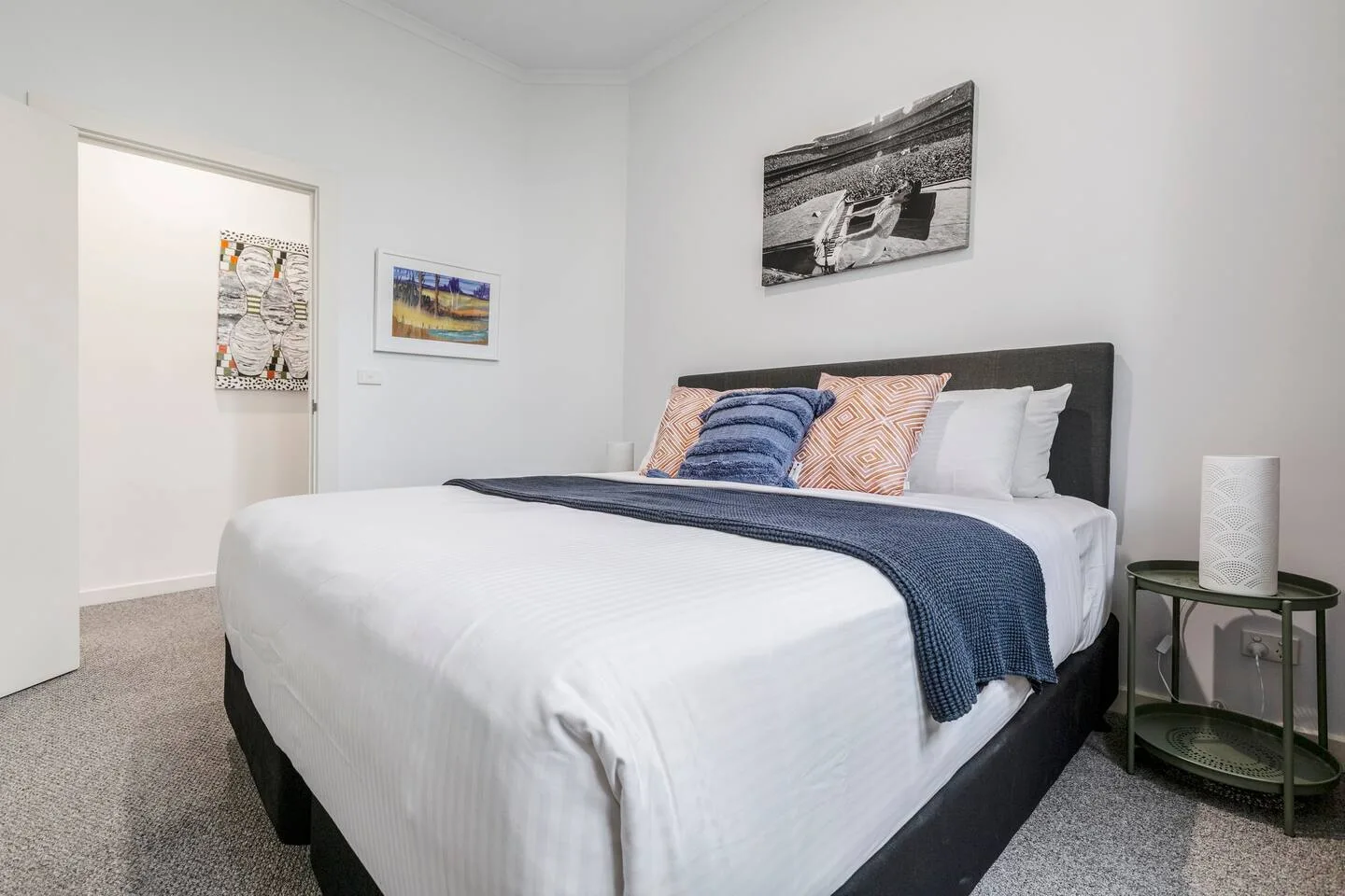 A bedroom with a neatly made bed, colorful pillows, and a framed picture above the headboard.