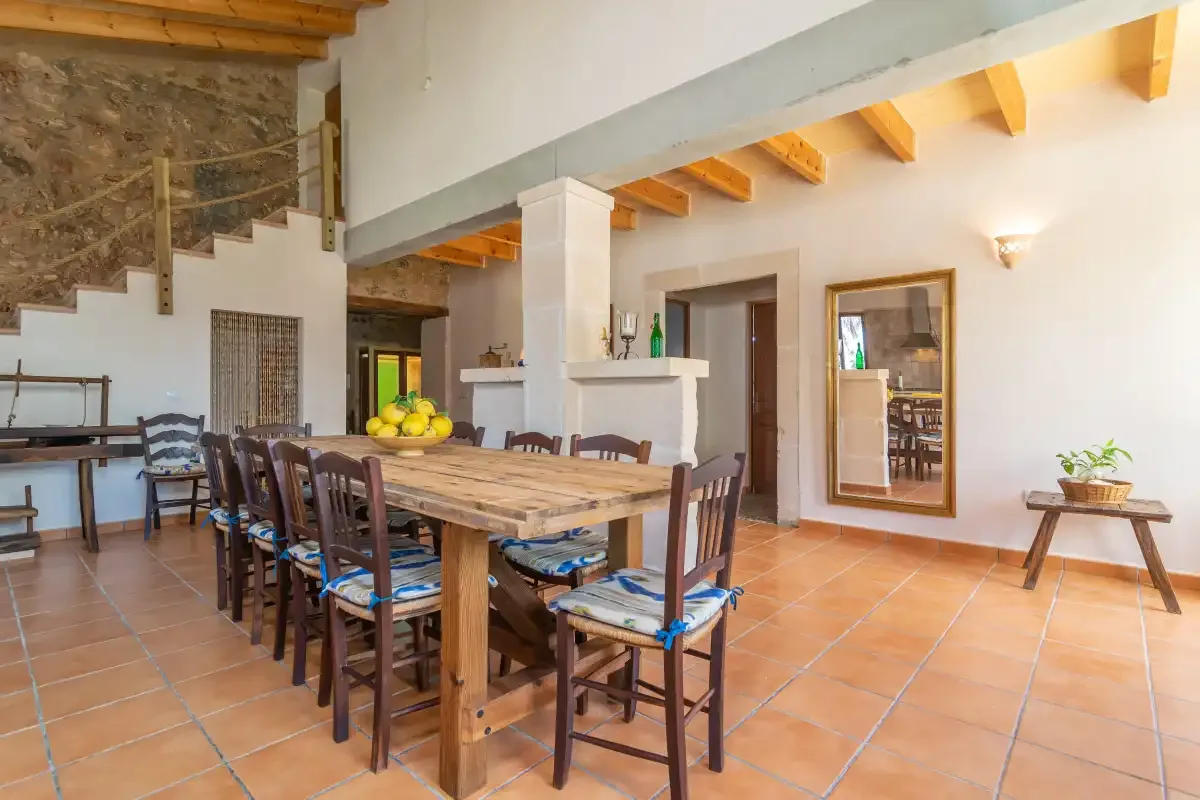 Comedor con una larga mesa de madera y sillas bajo vigas vistas.