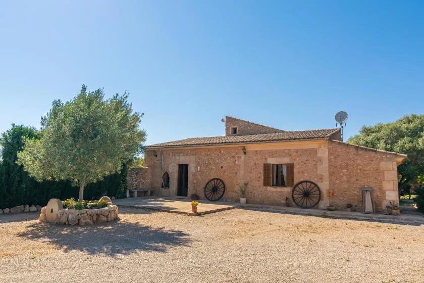 Una casa de piedra rústica se encuentra junto a un patio de grava y árboles frondosos.