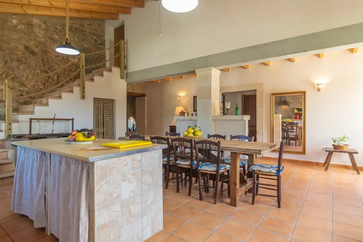 Cocina y comedor diáfanos con una mesa larga de madera y vigas vistas.